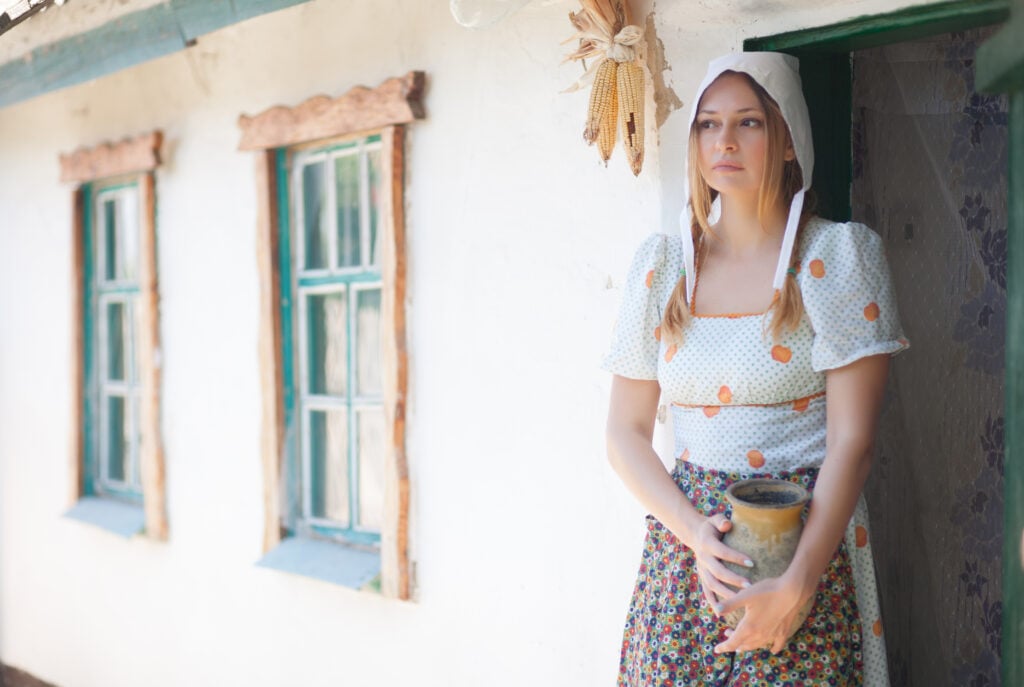 Woman young women on the background of a retro rural home with a jug in her hands.