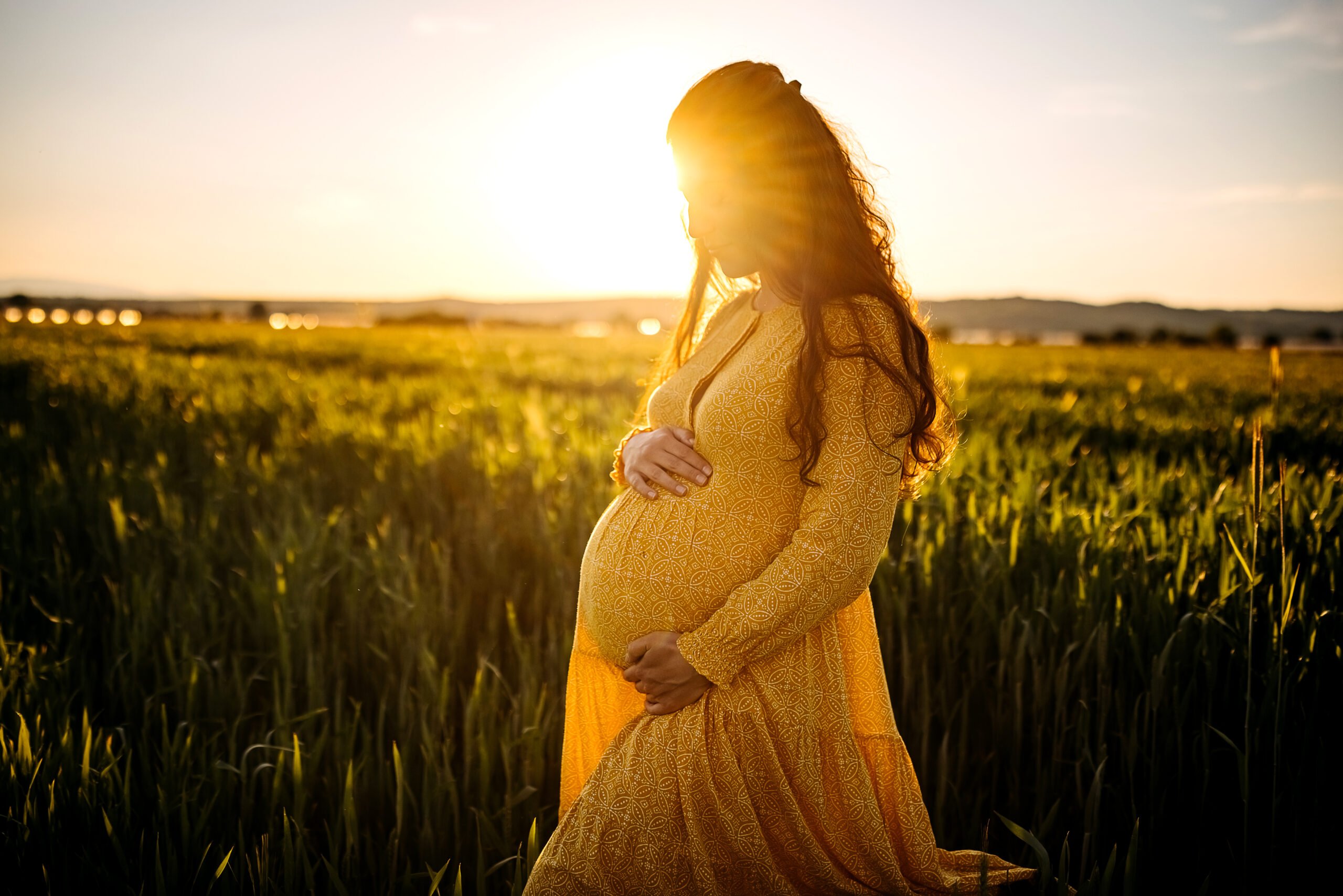 Pregnant woman holding stomach in middle of meadow
