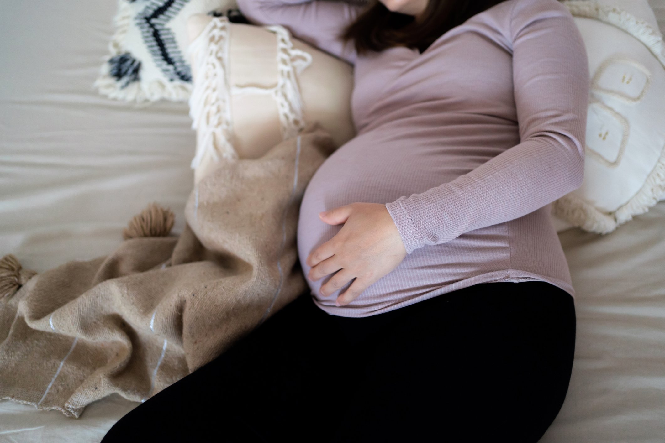 High angle shot of Asian pregnant woman holding her belly, sleeping on bed. Comfortable sleeping positions during pregnancy. Insomnia, sleeping disorder and physical discomfort during pregnancy