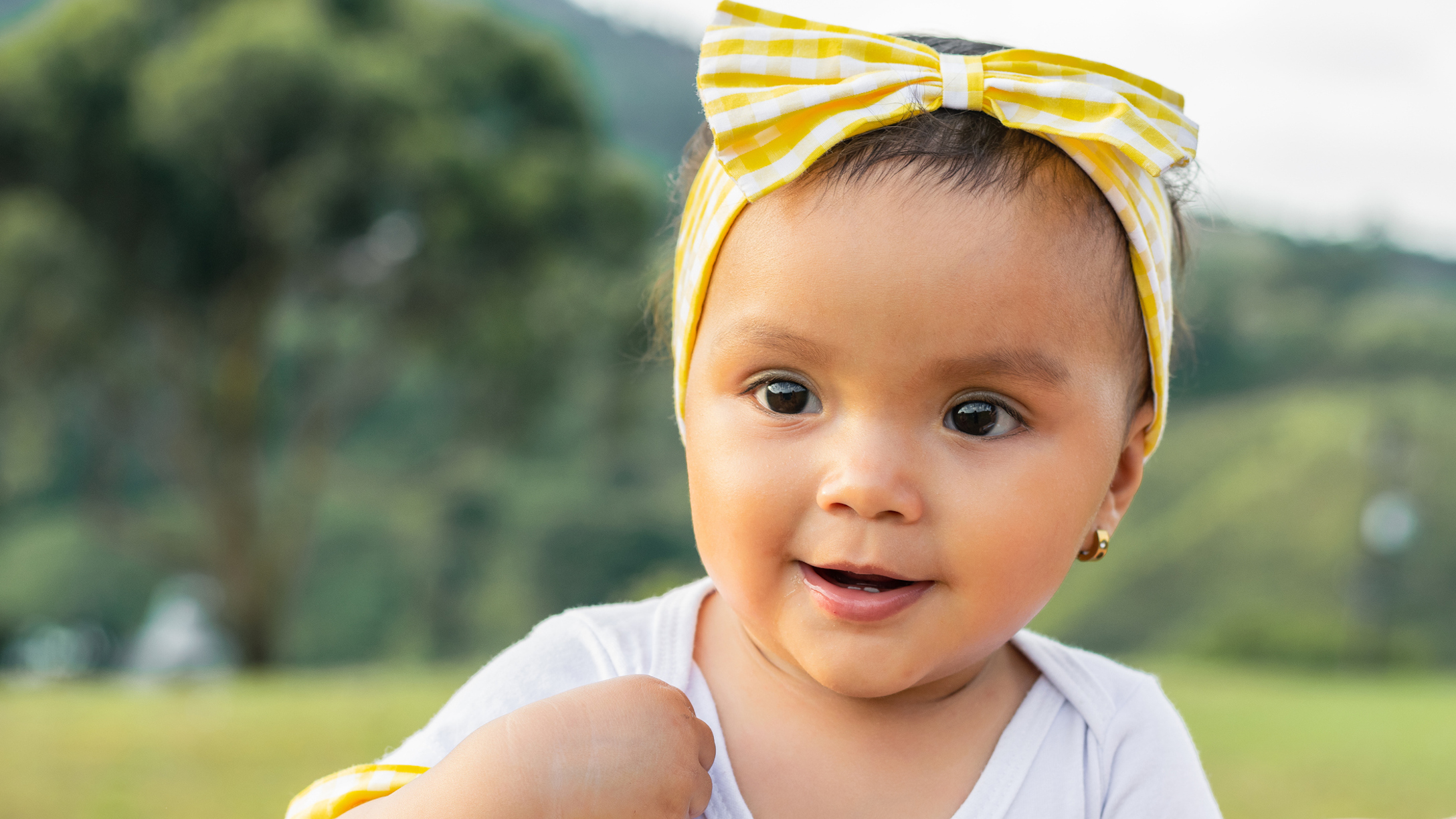 close up of a beautiful latina baby girl with brown skin smiling very happy. mother takes her daughter in her arms for a walk in the countryside on a nice summer day.