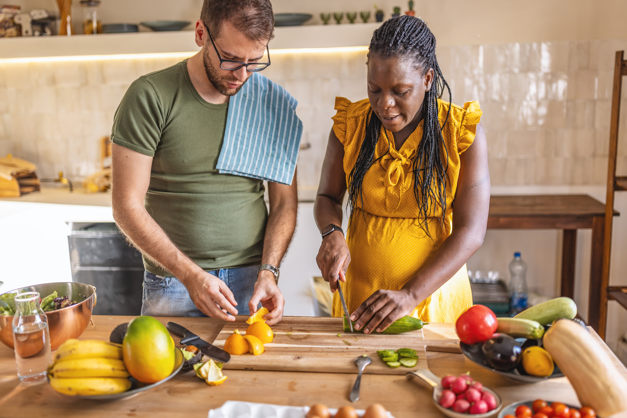 Photo of happy black pregnant woman and her husband preparing healthy food together in the kitchen.