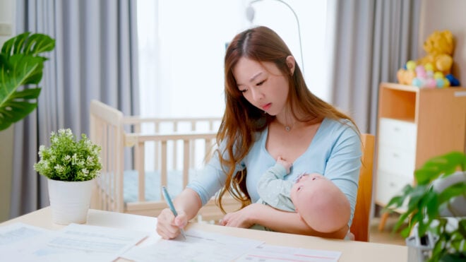 new mom holding newborn baby and writing
