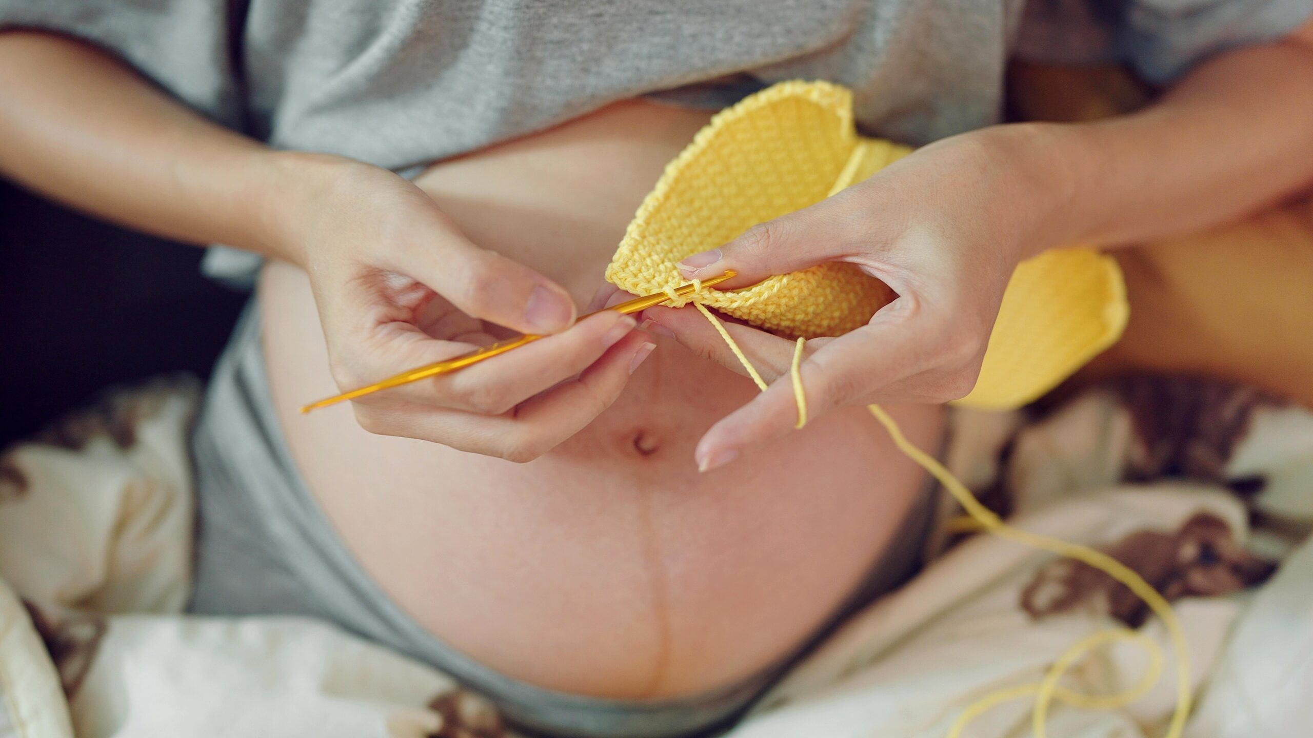 Women pregnant knitting handcraft clothes for her upcoming baby. Close up hands of pregnant woman doing knitting handcraft clothes for baby. Pregnancy concept