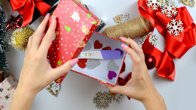 Woman's hands making a pregnancy test as a Christmas gift. table with New Year's decorations. View from above. Holiday mood, motherhood, waiting concept