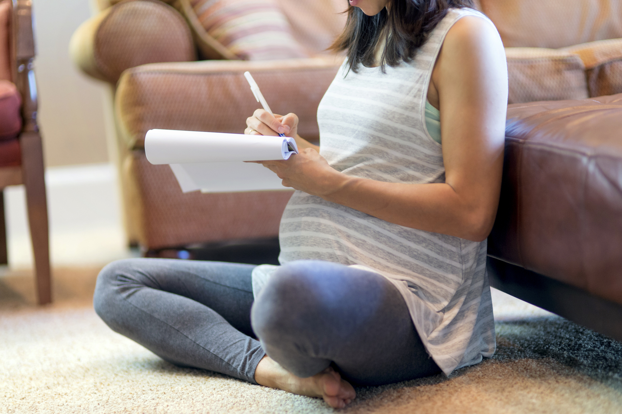 Pregnant mother sitting on carpet using a pad and paper